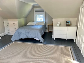 A bedroom with a bed, a dresser, a nightstand, a window, and a door.