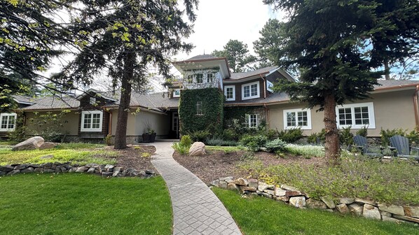 A two-story house with a stone foundation, a covered porch, and a landscaped front yard with a pathway. - Broadmoor Meeting House (Colorado Springs)