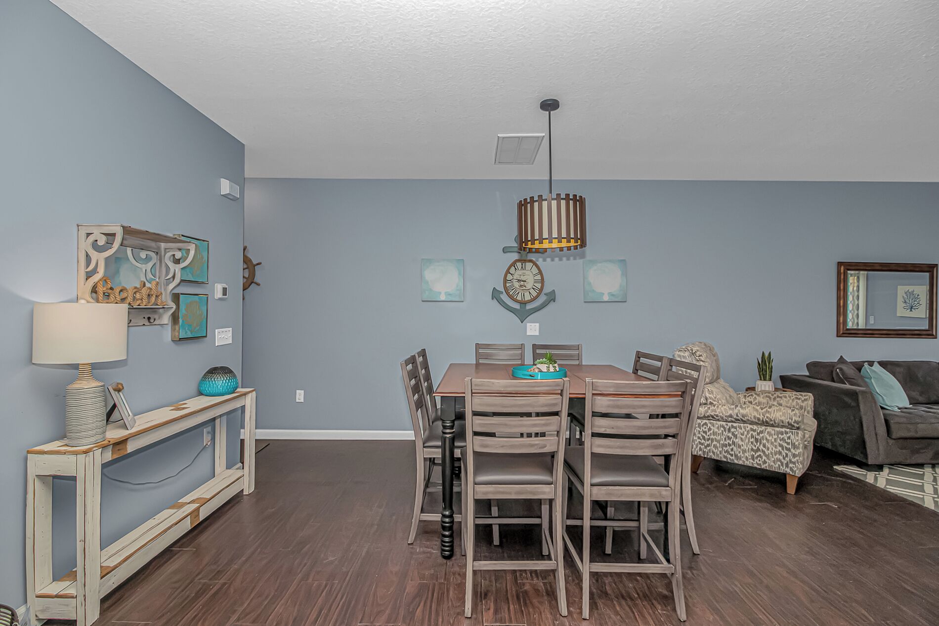 A dining area with a wooden table and chairs, a wall-mounted clock, and a ceiling light fixture.