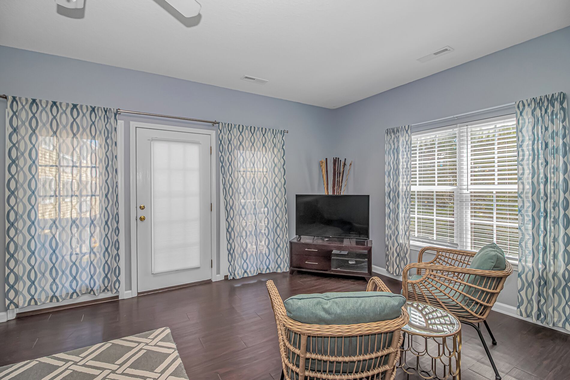 A living room with a TV, wicker chairs, a door, and patterned curtains.