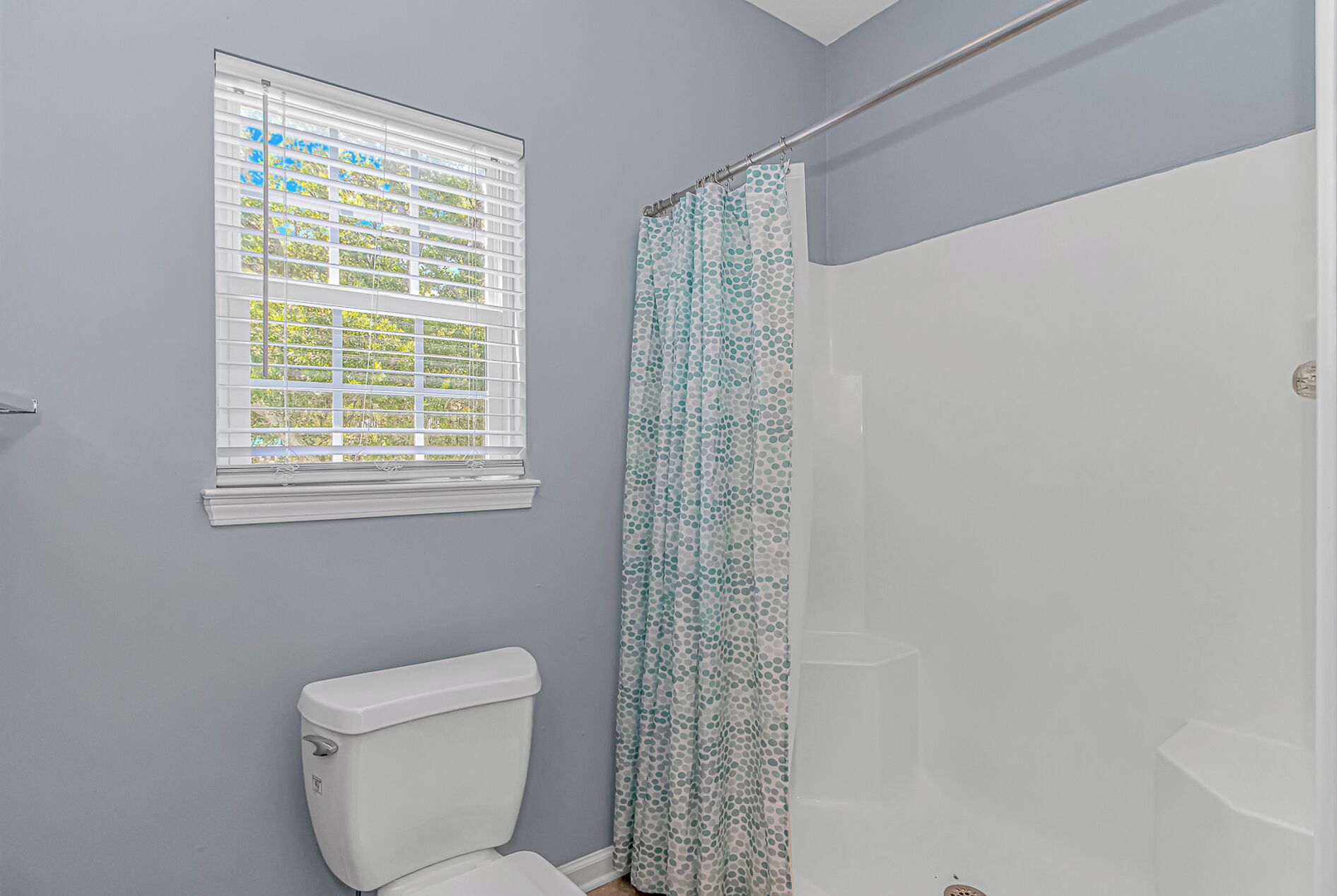 A bathroom with a toilet, a window with blinds, and a shower curtain.