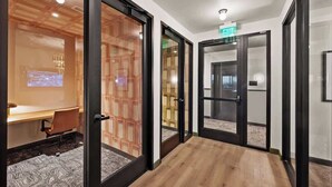 Un corridoio con porte in vetro, pavimento in legno e una sala conferenze con schermo proiettore.