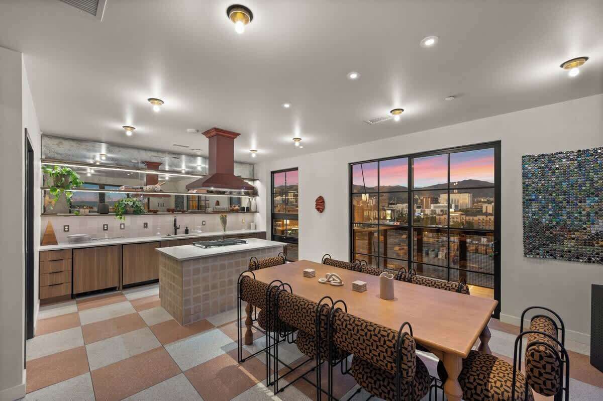 A modern kitchen with a dining area, large windows with a city view, and a decorative wall art piece.
