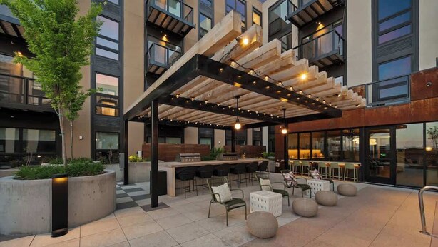 Area esterna con posti a sedere, pergola in legno, bar e arredi moderni.