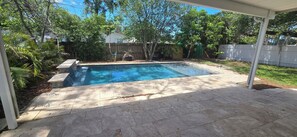 Un jardin avec une piscine, entouré d’arbres et délimité par une clôture en bois.