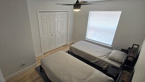 Ein Schlafzimmer mit zwei Betten, einem Deckenventilator, einem Fenster mit Jalousien und einer Tür.
