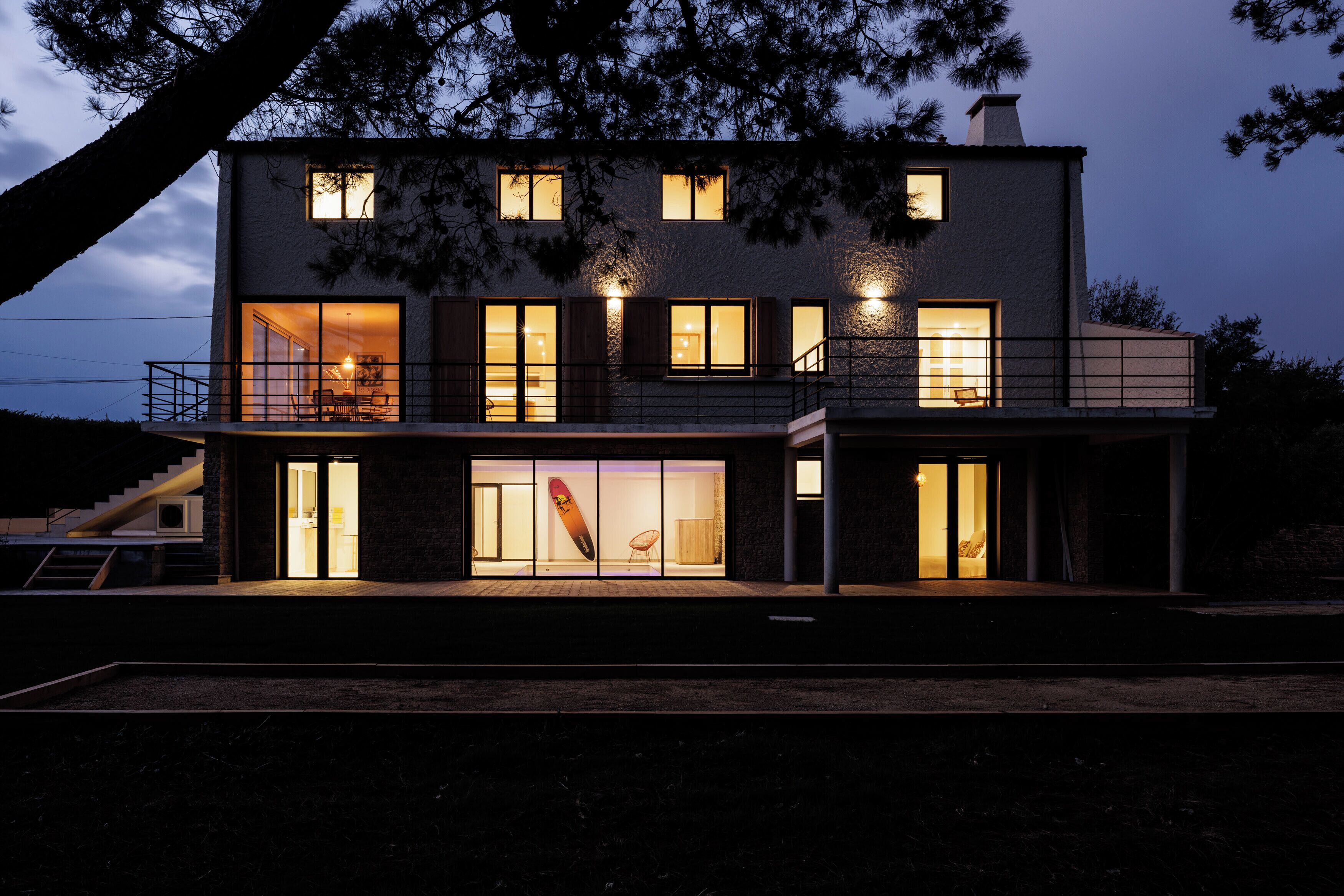 Une maison moderne à deux étages, dotée de grandes fenêtres, d’un balcon et d’un escalier.