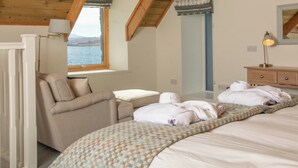 A bedroom with a bed, a chair, a nightstand, a lamp, a dresser, and a window with a view. - A secluded Skye boathouse where rugged beauty meets refined coastal living. (Skye)