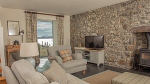 A living room with a stone wall, a television, a sofa, and a fireplace. - A secluded Skye boathouse where rugged beauty meets refined coastal living. (Skye)