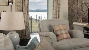A living room with a sofa, a lamp, a stone wall, and a view of mountains. - A secluded Skye boathouse where rugged beauty meets refined coastal living. (Skye)