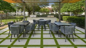 Un patio exterior con una pérgola, varias mesas y sillas, y un suelo con diseño.