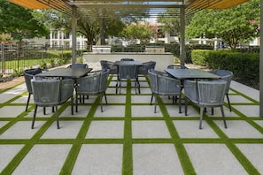 Eine Terrasse im Freien mit einer Pergola, mehreren Tischen und Stühlen sowie einem gemusterten Boden.