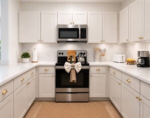 A kitchen with white cabinets, a microwave, a stove, and a toaster. - Designer Dream 3BR for Families & LongStays + Pool (Plano)