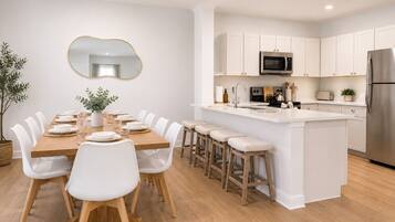 A modern kitchen with white cabinetry, a central island with stools, and a dining area with white chairs.