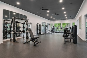 Ein Fitnessstudio mit unterschiedlichen Trainingsgeräten, großen Fenstern und Deckenventilatoren.