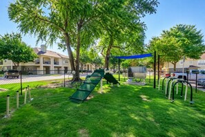 Ein Spielplatz mit Rutsche und Schaukeln, umgeben von Bäumen und einem Zaun.