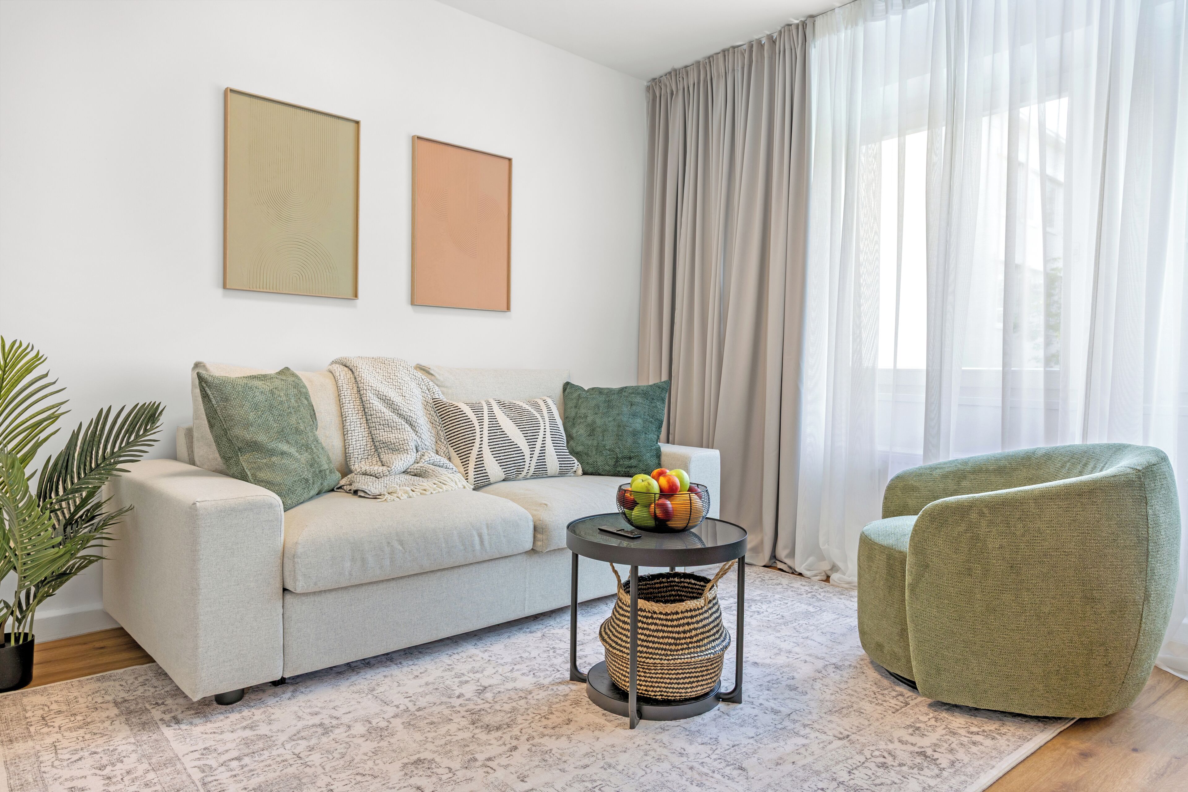 Un salon comprenant un canapé, une table basse ronde, un fauteuil vert et un panier en osier.