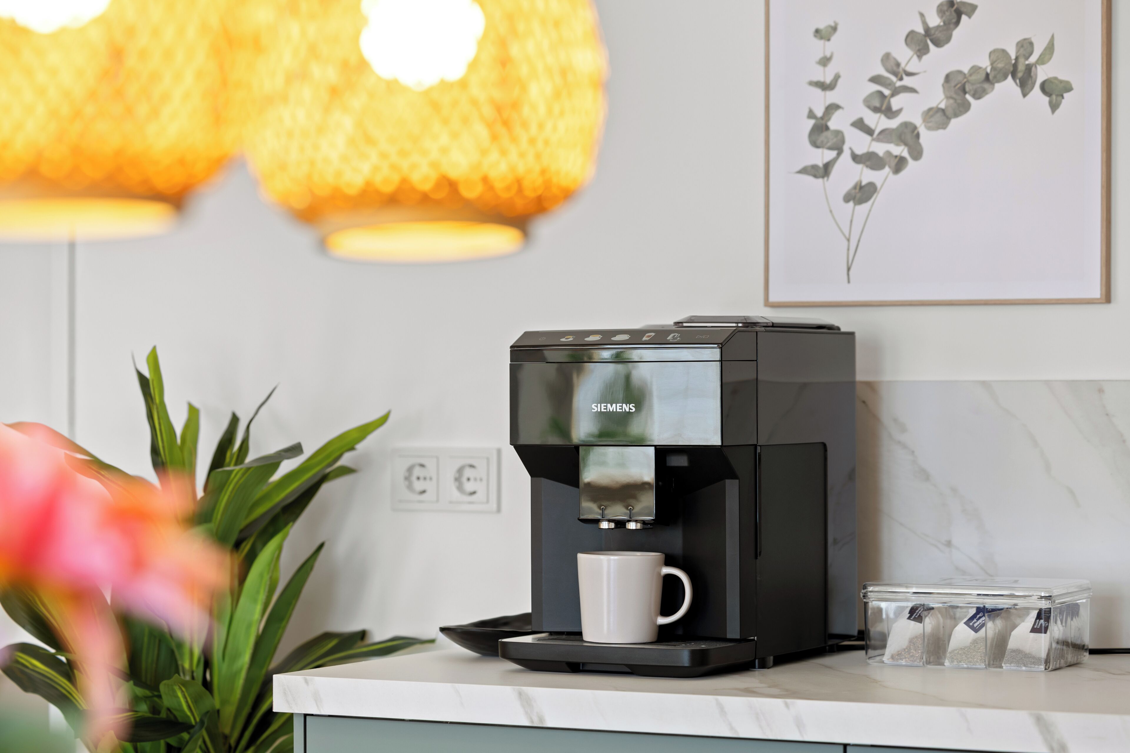 A modern kitchen with a coffee maker, a white mug, and a clear container with coffee pods.