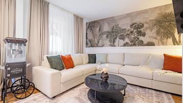 Una sala de estar con un sofá modular, una mesa de centro de vidrio, una máquina de palomitas de maíz y un mural grande en la pared.