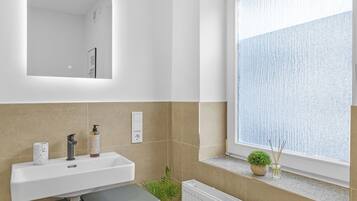 Een badkamer met een witte wastafel, een spiegel, een potplant en een raam met uitzicht.