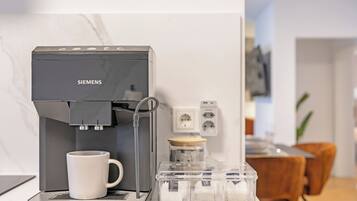 A Siemens coffee machine with a white mug, a clear container with coffee pods, and a power outlet in a modern kitchen setting.