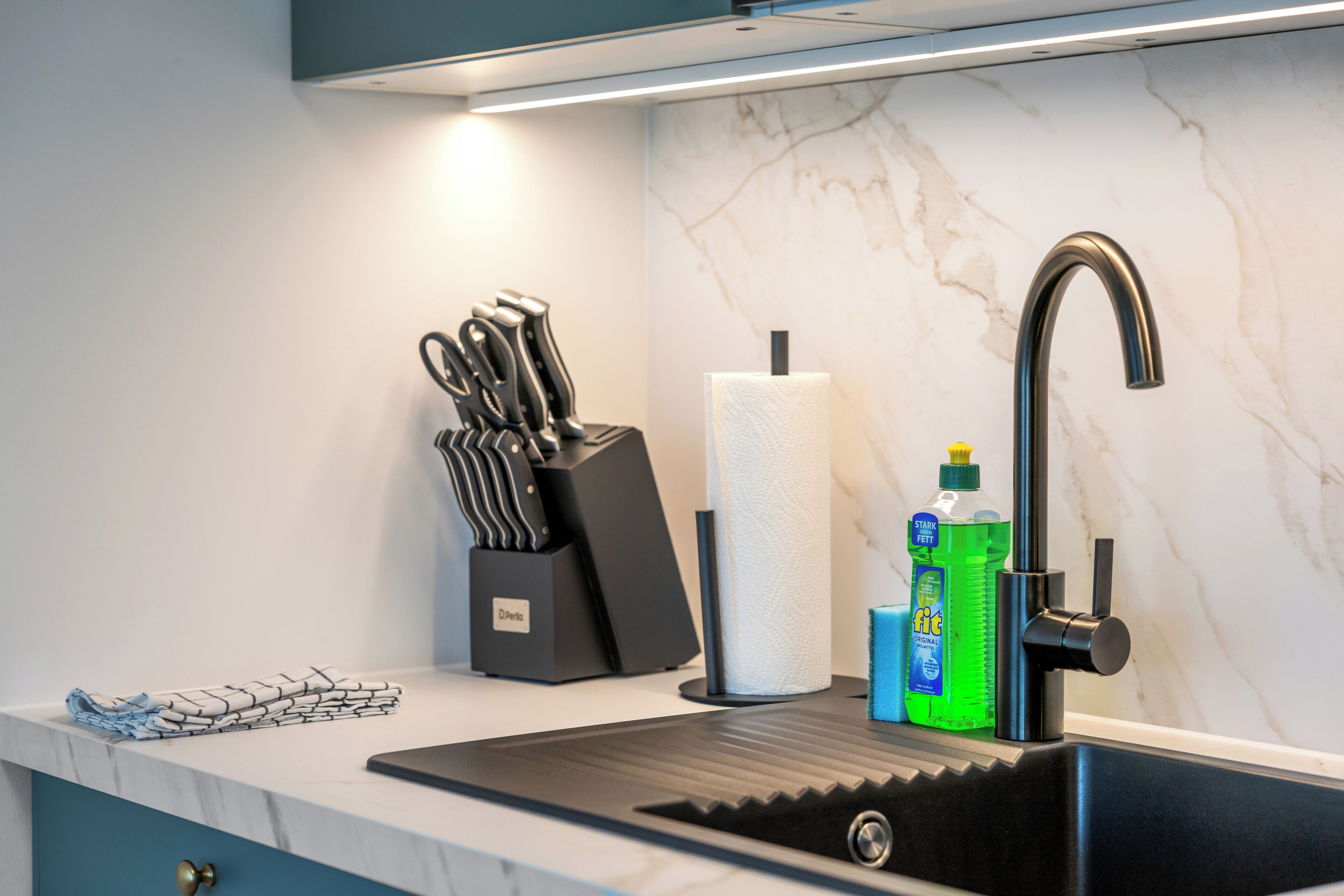 Una cocina moderna con un lavamanos negro, salpicadero de mármol y grifo de acero inoxidable.