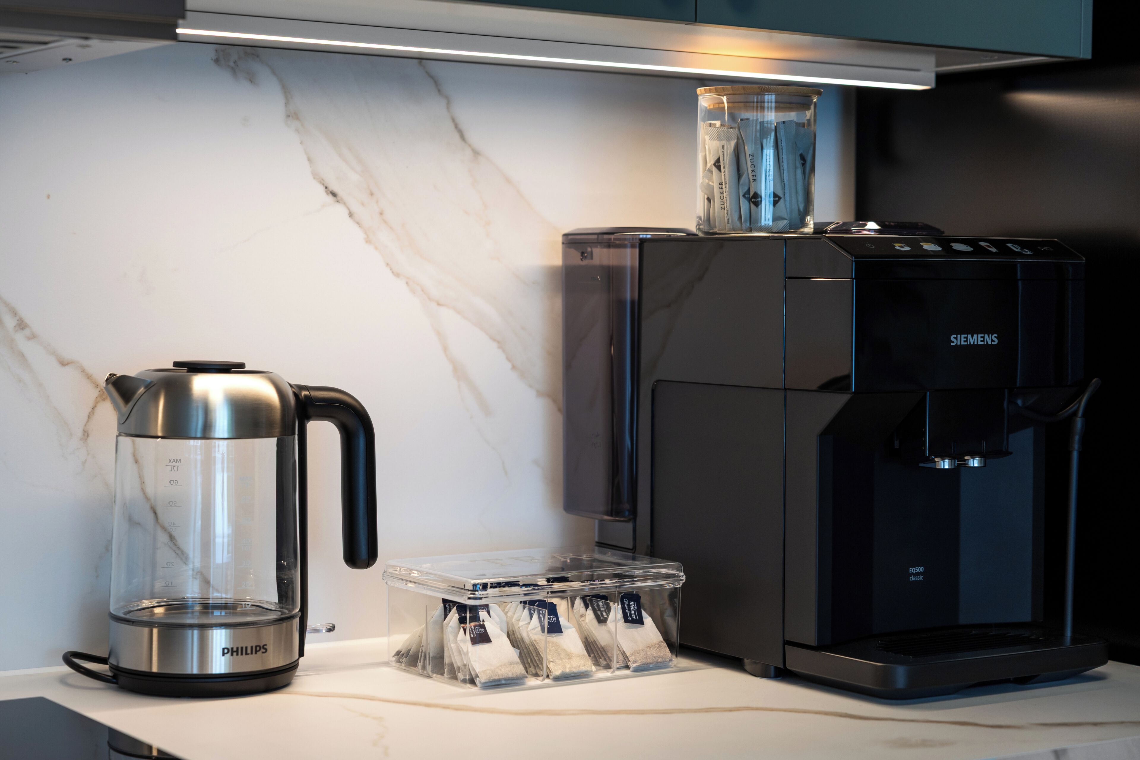 Une cuisine équipée d’une machine à café, d’une bouilloire et d’une boîte de sachets de thé.