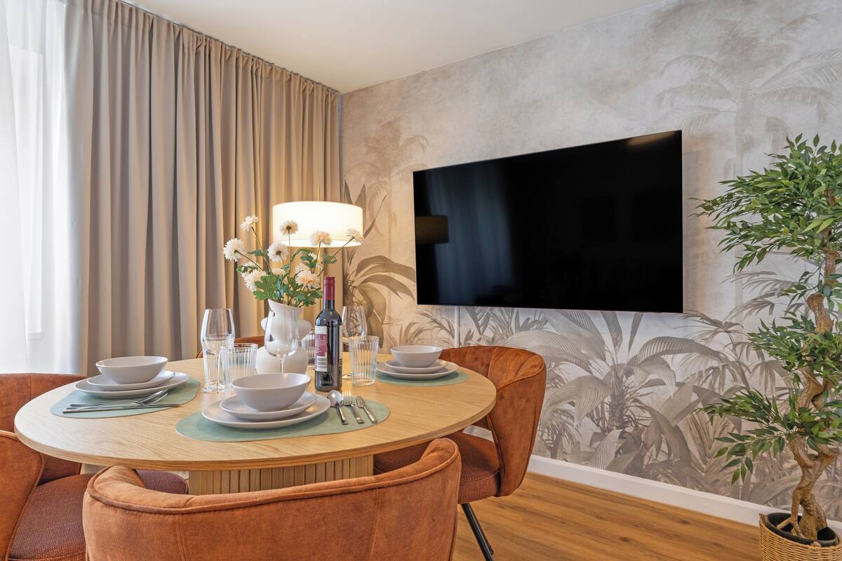 A dining area with a round table, chairs, a TV mounted on the wall, and a potted plant.