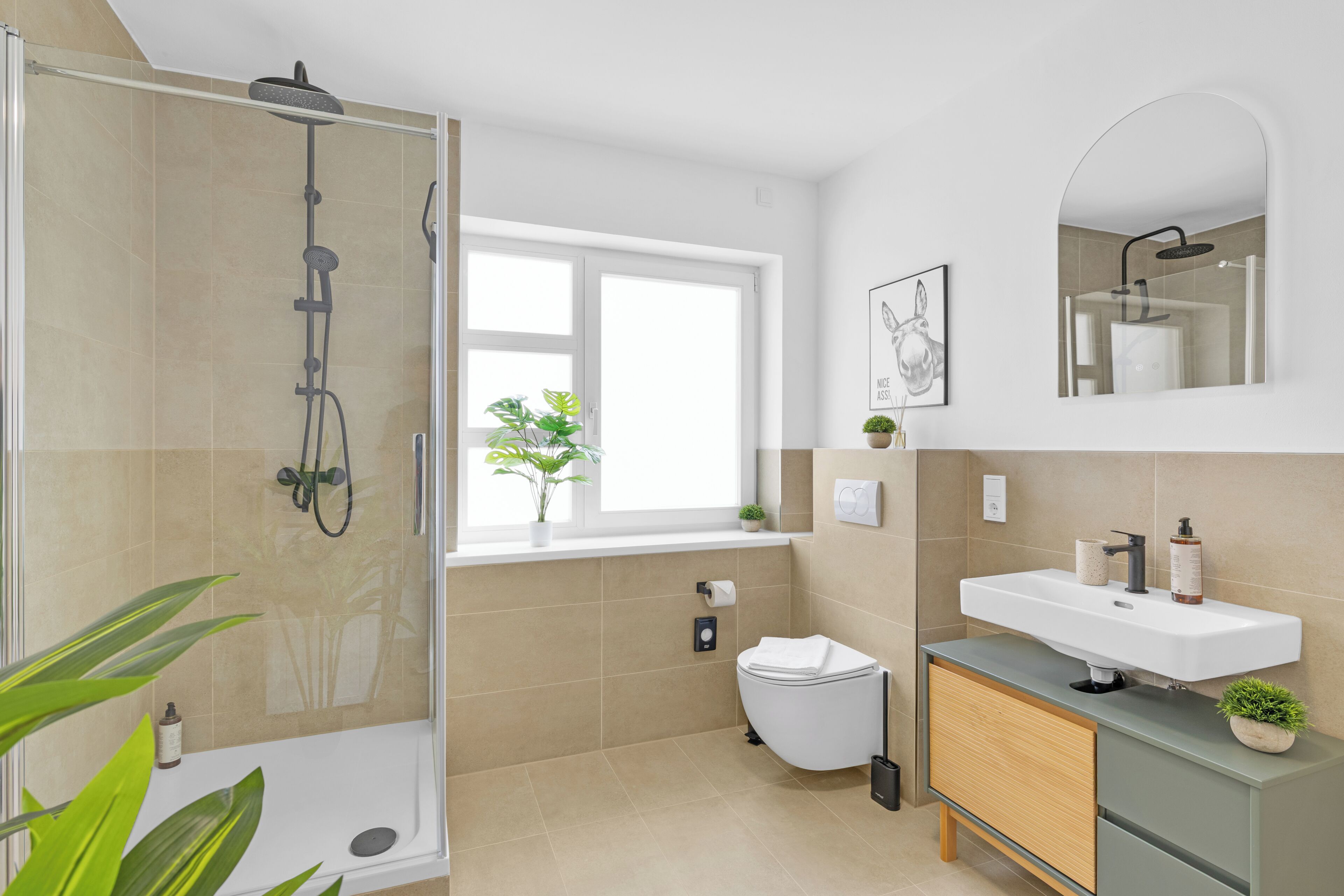 A modern bathroom with a glass-enclosed shower, a white toilet, a sink with a mirror, and a window with a plant.