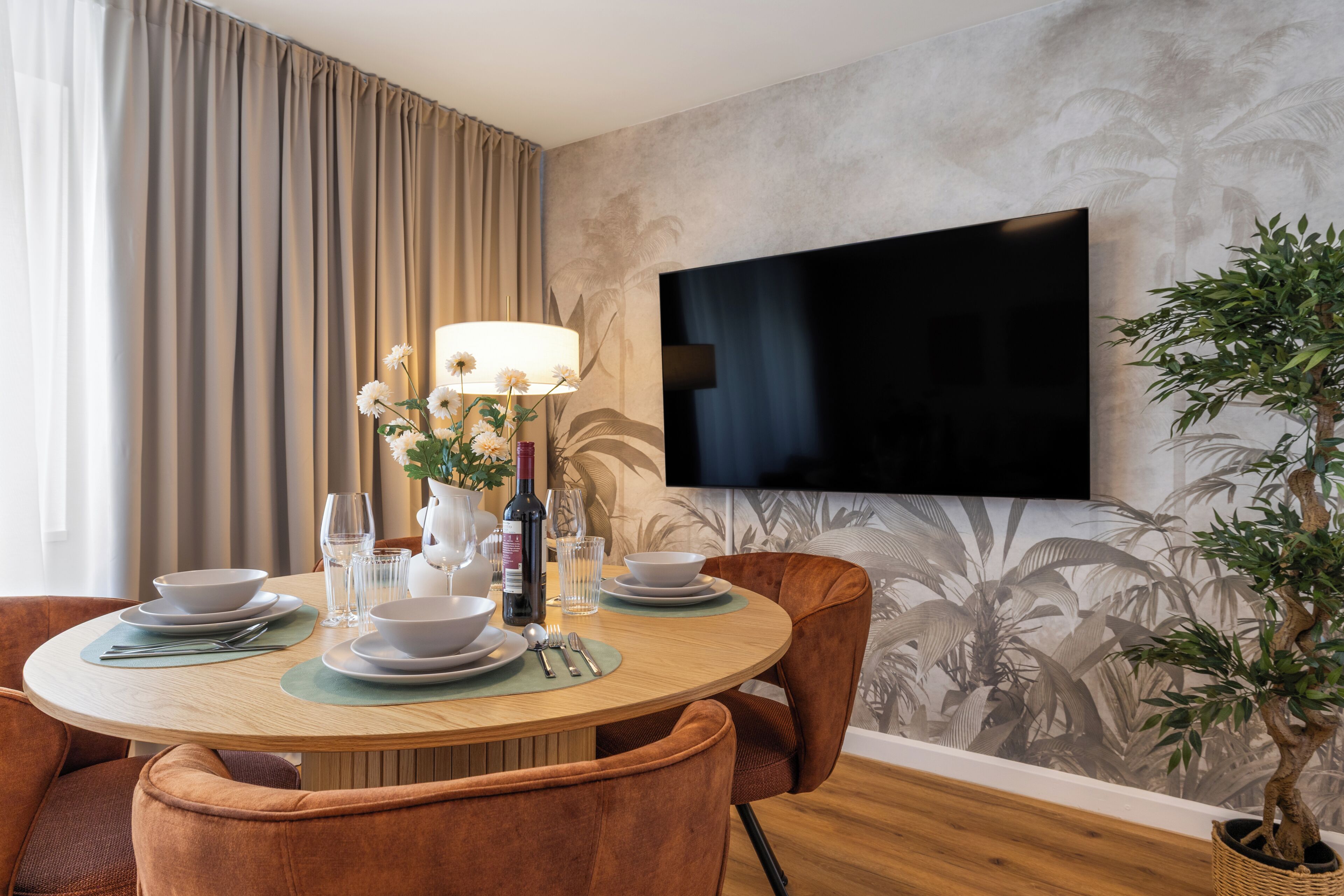 A dining area with a round table, chairs, a flat-screen TV, and a potted plant.