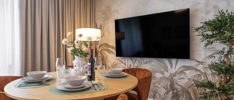 A dining area with a round table, chairs, a flat-screen TV, and a potted plant.
