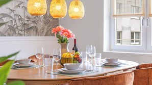 A dining area with a round table set for four, a vase with flowers, and a fruit bowl. - Svyvo Bonn - City Apartments (Bonn)