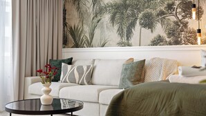 A modern living room with a sofa, a round coffee table, and a wall mural of tropical foliage. - Svyvo Bonn - City Apartments (Bonn)