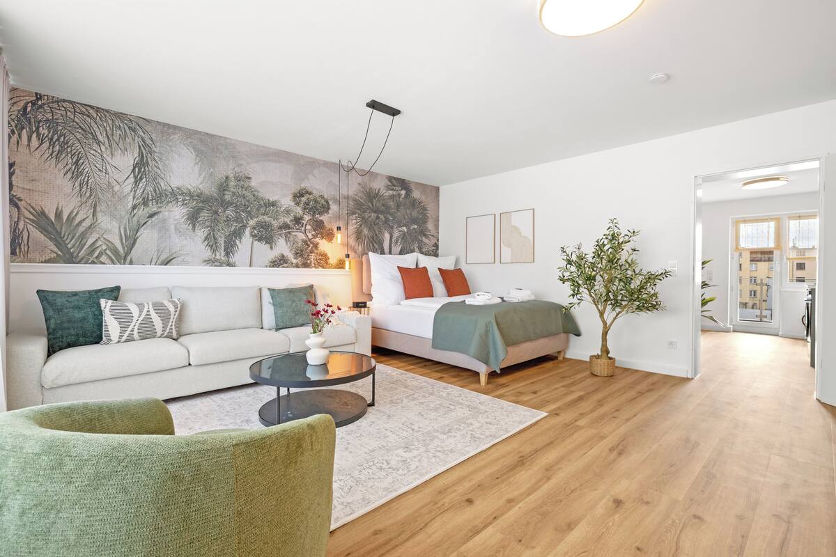 A modern living room with a sofa, a coffee table, a bed, and a large wall mural.