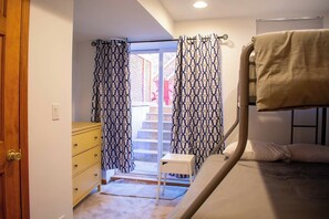 Ein Schlafzimmer mit Etagenbett, Holztür, gelbem Schminktisch und gemusterten Vorhängen.