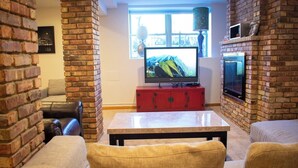 Ein Wohnzimmer mit Backsteinwand, einem Fernseher auf einem Schrank, einer Couch und einem Couchtisch.