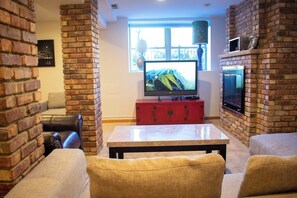Ein Wohnzimmer mit Backsteinwand, einem Fernseher auf einem Schrank, einer Couch und einem Couchtisch.