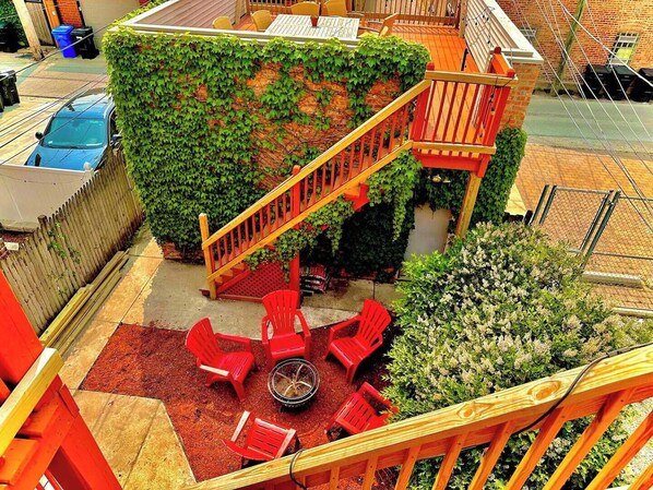 Eine Dachterrasse mit einer Holztreppe, roten Stühlen und einer Feuerstelle.