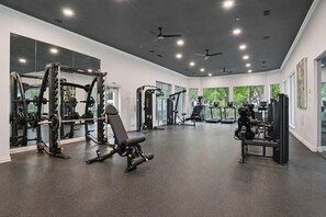 Een sportschool met diverse fitnessapparaten, grote ramen en plafondventilatoren.