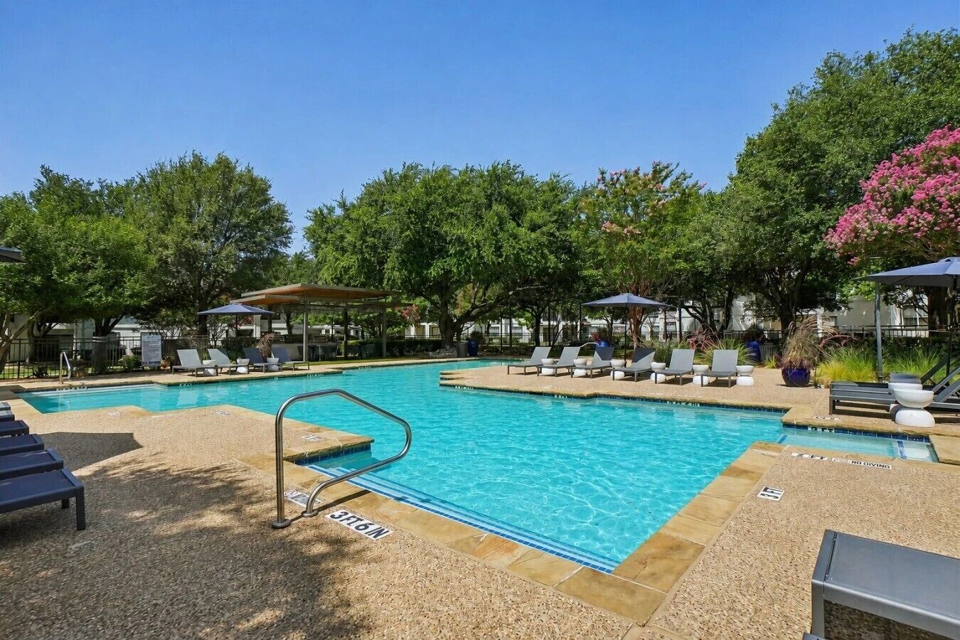 A rectangular outdoor swimming pool with a diving board, surrounded by lounge chairs and umbrellas.