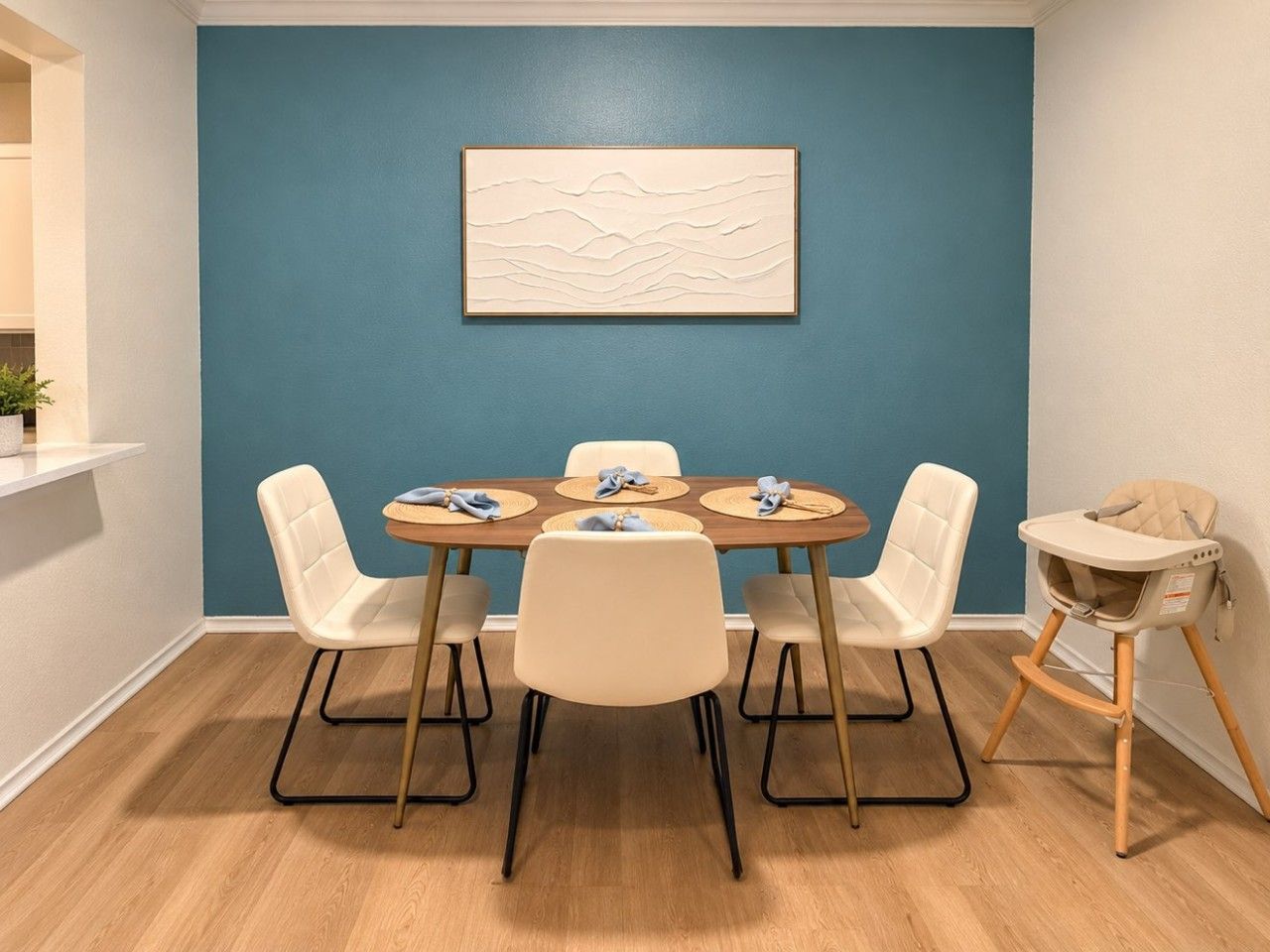 Een eetruimte met een blauwe accentmuur, een ronde tafel, vier stoelen en een kinderstoel.