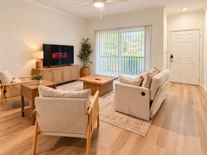 Een moderne woonkamer met een flatscreen televisie, een bank, een salontafel en een eethoek.