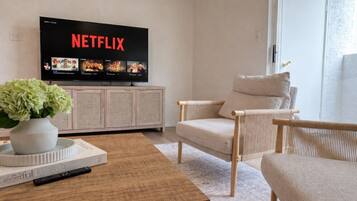 A living room with a television displaying Netflix, a sofa, a coffee table, and a bookshelf.