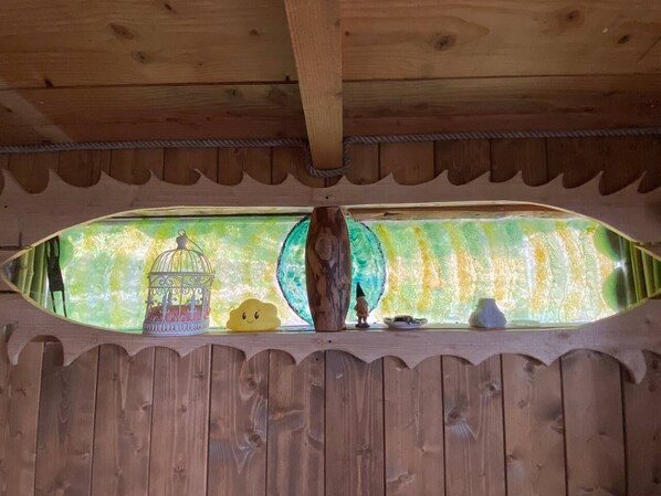 Una estructura de madera con una ventana, una jaula de pájaros, una figurita pequeña y un jarrón decorativo.