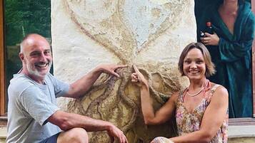 Eine große Steinsäule mit herzförmiger Reliefdarstellung, eine Person deutet darauf, und eine andere Person sitzt daneben.