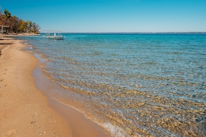 Ein Strand mit klarem Wasser, einer Mole und einer fernen Küstenlinie.
