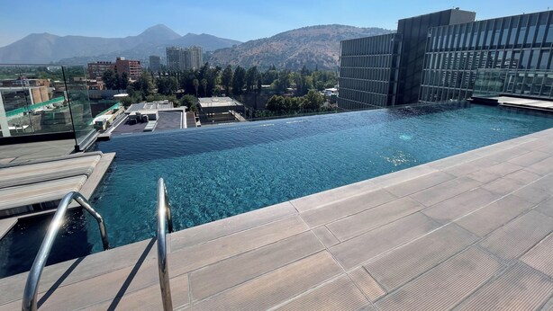 Una piscina infinita en la azotea con vistas despejadas a montañas y edificios al fondo.