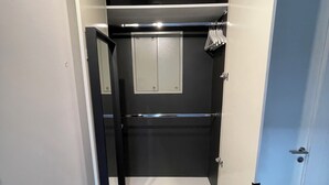 Un pasillo estrecho con una puerta que da a una habitación con un espejo, un interruptor de luz y un enchufe en la pared.