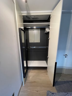 A narrow hallway with a door leading to a room with a mirror, a light switch, and a power outlet on the wall.