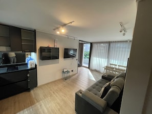 A modern living room with a sofa, a flat-screen TV, a coffee table, and a dining area with chairs.